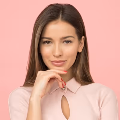 Young woman with long brown hair, wearing a pale pink top, resting her chin on her hand against a pink background.