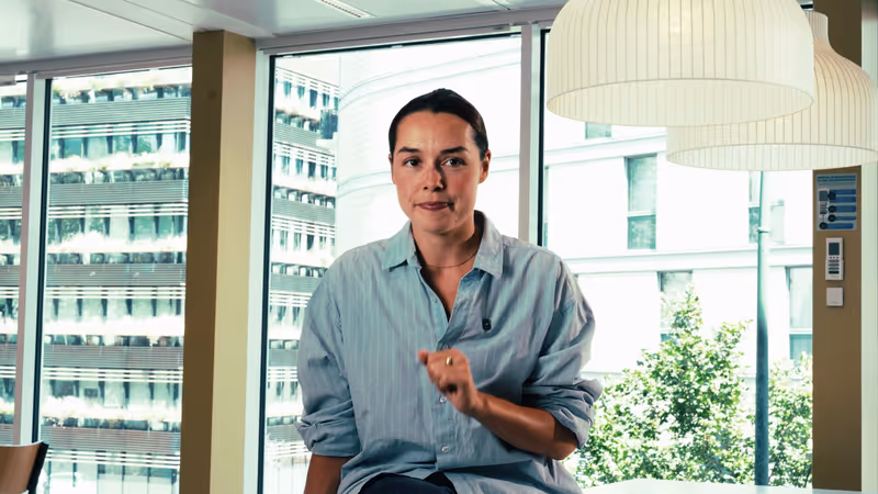 Femme en chemise claire s'adressant à la caméra dans un bureau lumineux, image d'ouverture de la vidéo de présentation Design Elite.